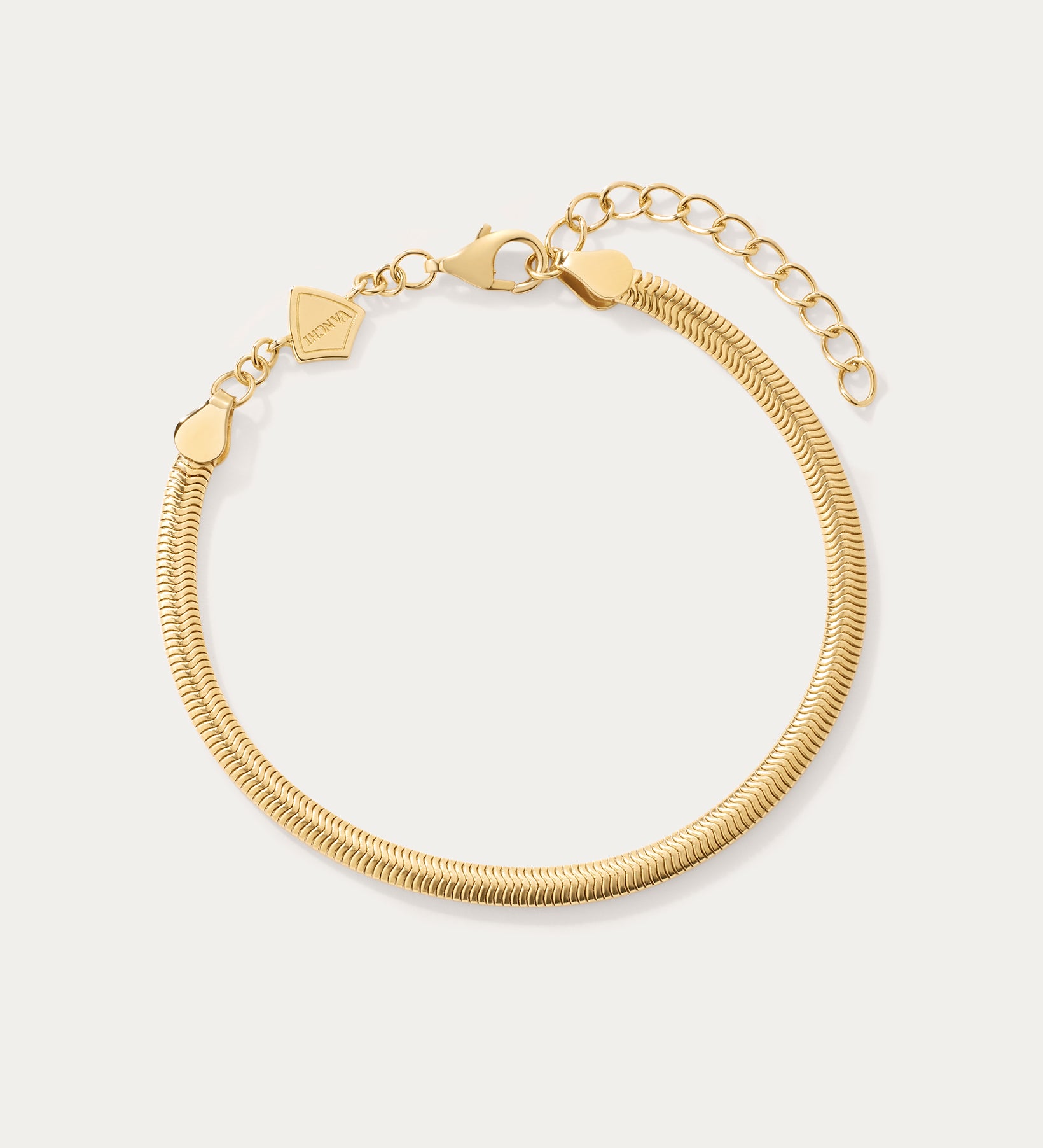 The Estelle Herringbone Chain Bracelet in Gold is a 3mm bracelet with an adjustable clasp, extension chain, and a small flat charm, perfect for bracelet stacking and shown on a light background.