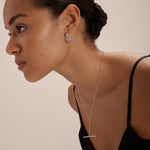 A woman with smooth, pulled-back hair wears a black spaghetti strap top and Esther Square Hoop Stud Earrings in Silver, paired with a delicate silver bar necklace, posing against a plain light background.