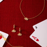 Silver Defender Evil Eye Necklace arranged with matching gold jewelry—bracelet, earrings, and charms—on a red textured surface, surrounded by playing cards like the ace of hearts and king.