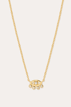 The Defender Evil Eye Necklace in Gold features an 18k gold-plated eye-shaped pendant with a central cubic zirconia and four dangling crystals, shown on a plain white background.