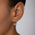 Close-up of an ear adorned with multiple gold earrings, featuring Defender Evil Eye Hoops in Gold with pearl details on the lobe and small protective jewelry along the cartilage.