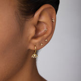 Close-up of an ear adorned with multiple gold earrings, featuring Defender Evil Eye Hoops in Gold with pearl details on the lobe and small protective jewelry along the cartilage.