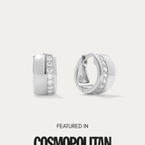 The Juni Pavé Chunky Huggie Earrings in Silver, hypoallergenic and perfect for daily wear, feature a vertical row of sparkling cubic zirconia and are displayed on a white background above the words "Featured in Cosmopolitan.