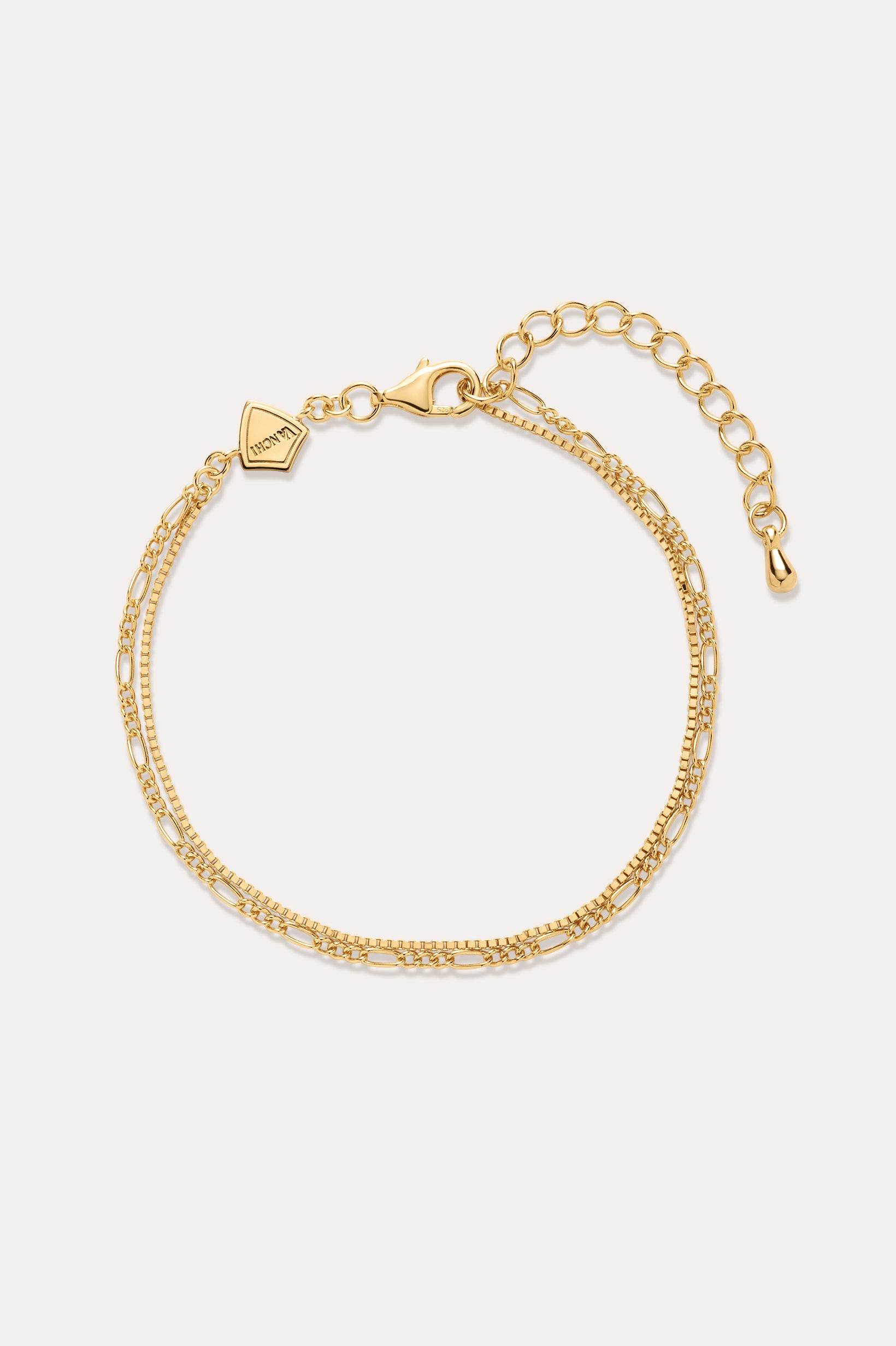 The Figaro And Box Chain Layered Bracelet in 18k Gold Plated features two intertwined strands in a mini Figaro box chain design with a lobster clasp, adjustable extender, and geometric tag, shown on a plain off-white background.