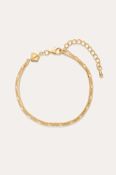 The Figaro And Box Chain Layered Bracelet in 18k Gold Plated features two intertwined strands in a mini Figaro box chain design with a lobster clasp, adjustable extender, and geometric tag, shown on a plain off-white background.