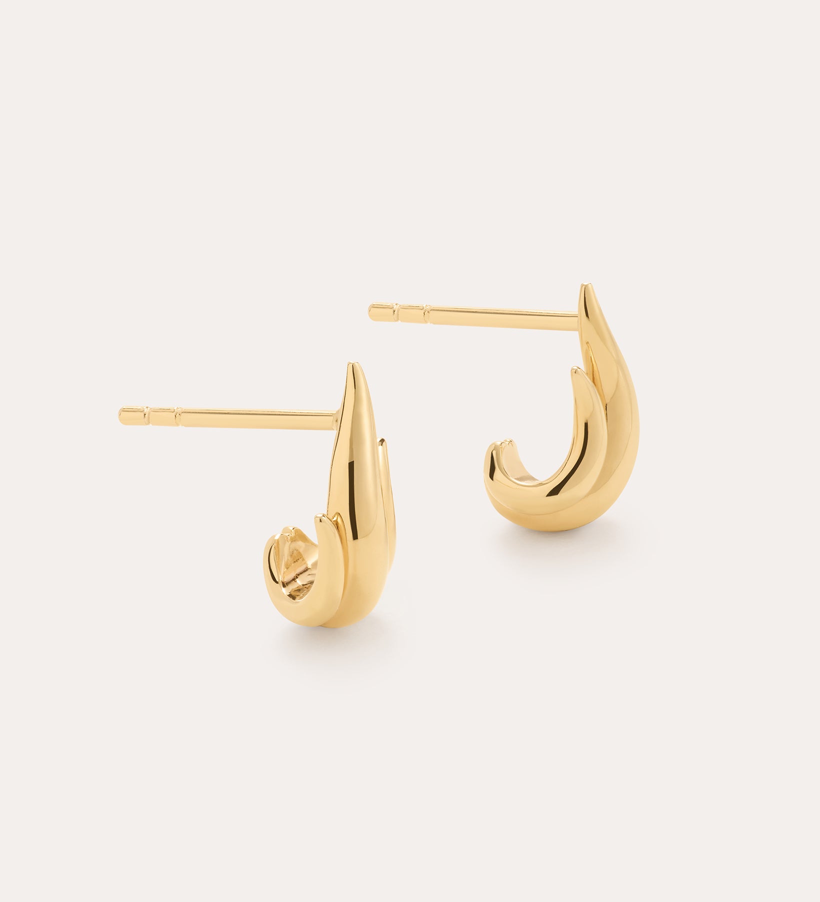 The Flame Stud Earrings in Gold are a shiny, 18k gold plated, crescent-shaped pair shown on a plain light background—one lying flat and the other upright to highlight their sculptural design and post backs.