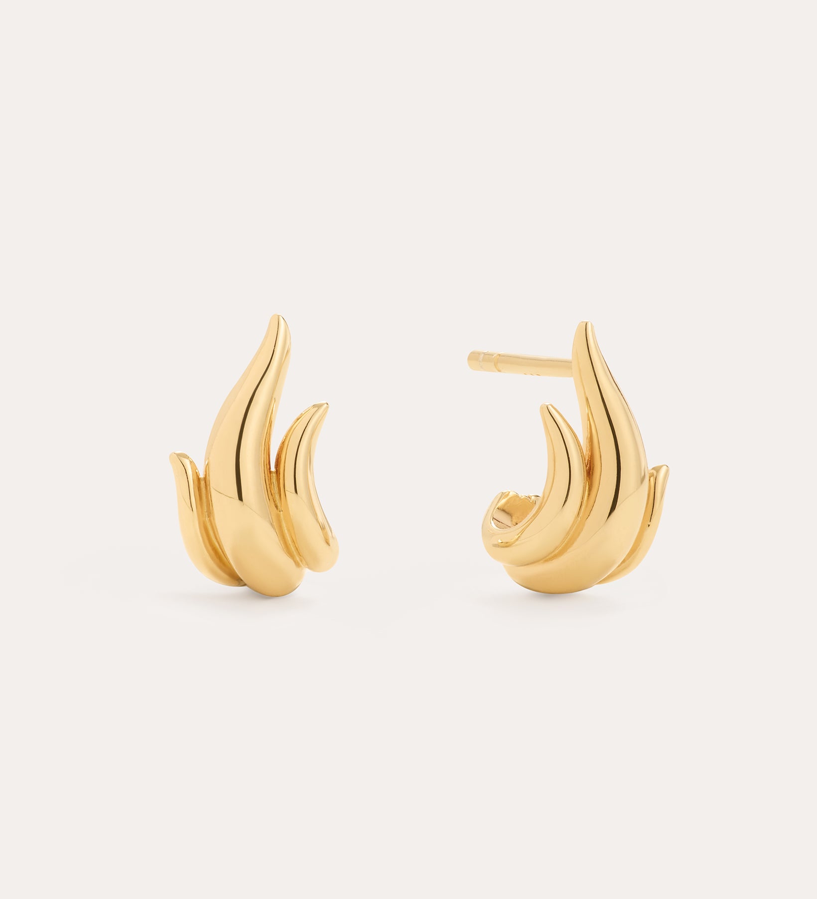 The Flame Stud Earrings in Gold, crafted with 18k gold plating and shaped like abstract flames, are shown against a neutral background—one earring displays the front view, while the other reveals the sculptural side and post.