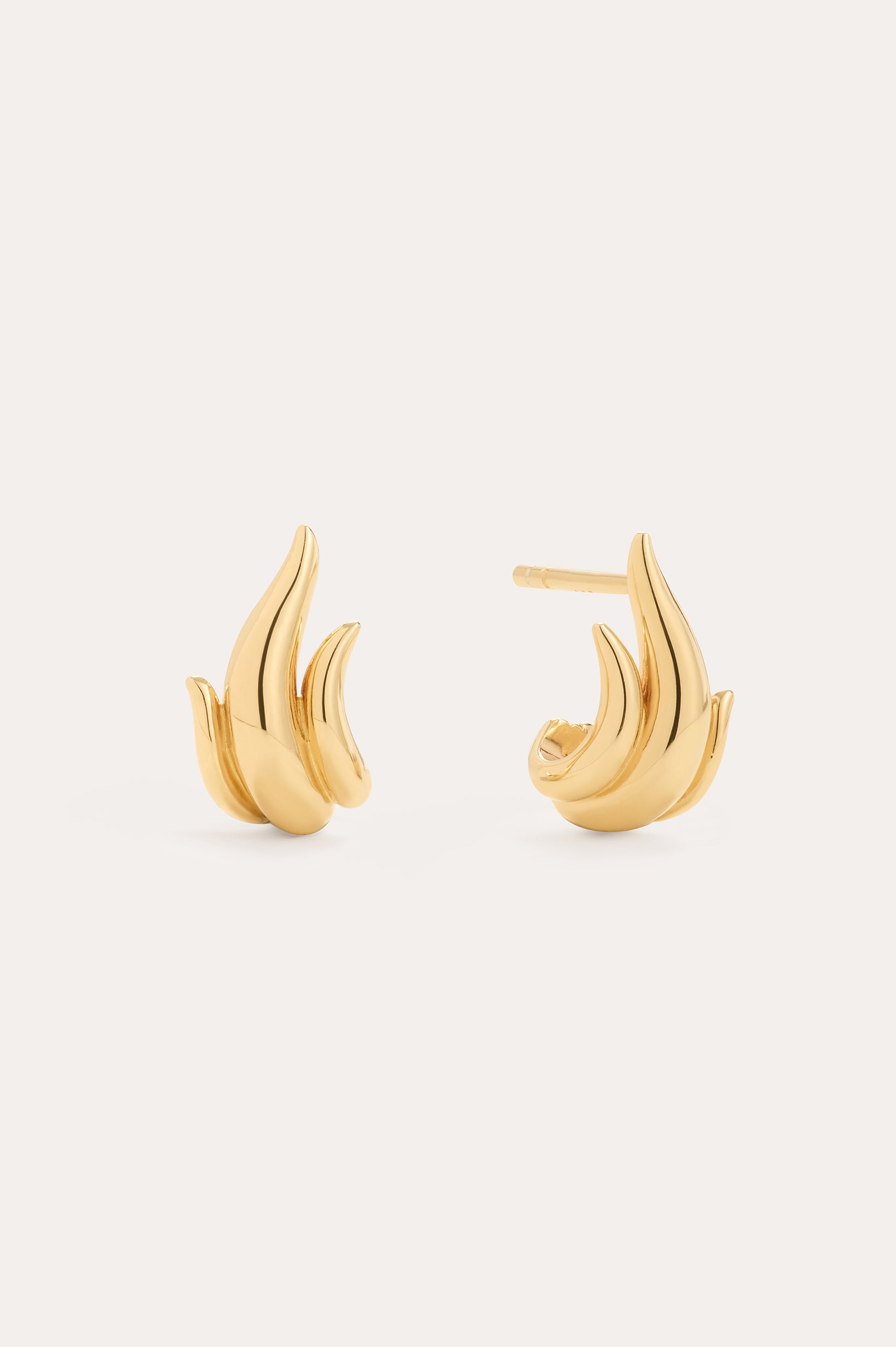 The Flame Stud Earrings in Gold, crafted with 18k gold plating and shaped like abstract flames, are shown against a neutral background—one earring displays the front view, while the other reveals the sculptural side and post.