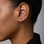 Close-up of a woman wearing Flame Stud Earrings in Gold—small, 18k gold-plated multi-bar studs. Her dark hair is pulled back, she's in a black collared top, and the background is soft and neutral.