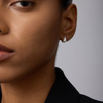 Close-up of a person with medium brown skin wearing Flame Stud Earrings in Silver and a black blazer, hair pulled back, with only the left side of their face visible.