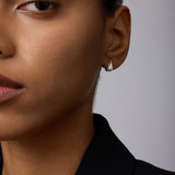 Close-up of a person with medium brown skin wearing Flame Stud Earrings in Silver and a black blazer, hair pulled back, with only the left side of their face visible.