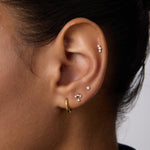 Close-up of a person's ear with multiple piercings, showcasing three Freda Lab-grown Diamond Flat Back Studs in 14K solid yellow gold on the upper and middle ear, plus a gold hoop on the lobe. The person has short dark hair.