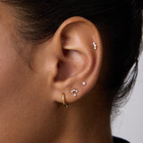 Close-up of a person's ear with multiple piercings, showcasing three Freda Lab-grown Diamond Flat Back Studs in 14K solid yellow gold on the upper and middle ear, plus a gold hoop on the lobe. The person has short dark hair.
