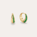 The Georgie Crystal Knife Edge Huggie Hoop Earrings in Green feature small gold hoops with a row of green crystals along the front, shown against a plain light background.