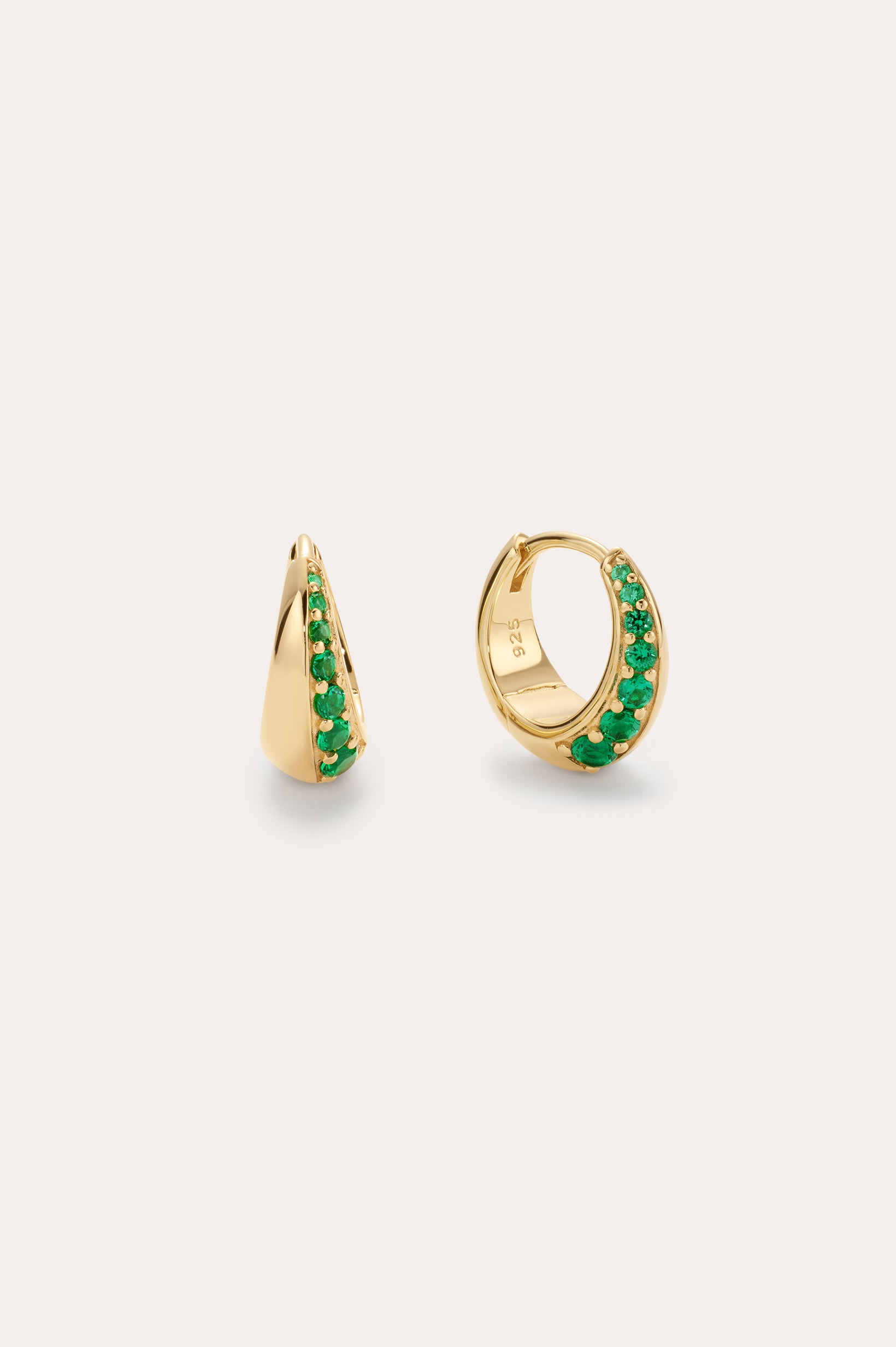 The Georgie Crystal Knife Edge Huggie Hoop Earrings in Green feature small gold hoops with a row of green crystals along the front, shown against a plain light background.