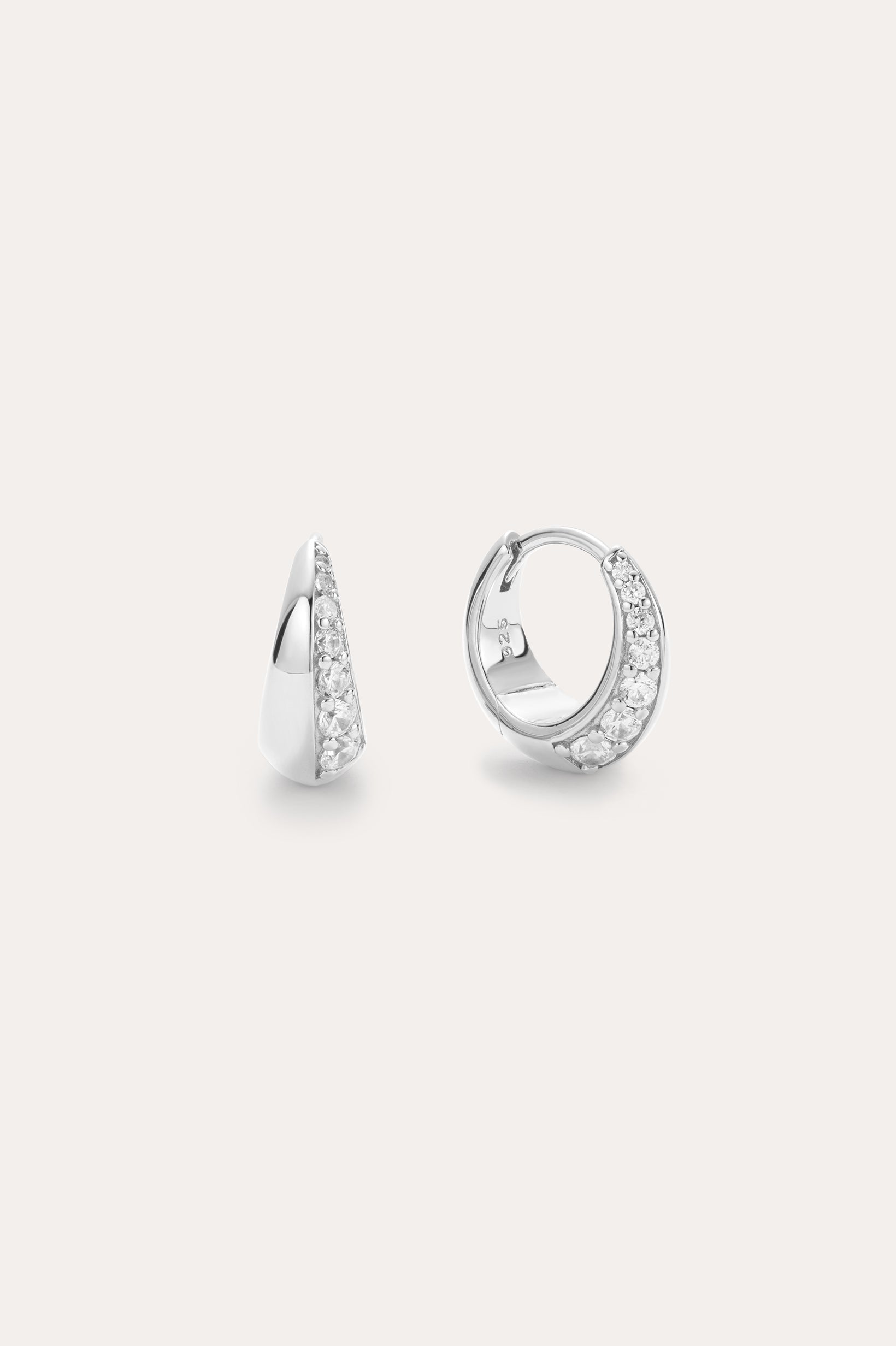 The Georgie Crystal Knife Edge Huggie Hoop Earrings in Silver feature a row of sparkling white stones, shown on a plain light background with one earring displayed from the front and the other from the side.