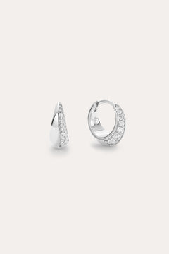 The Georgie Crystal Knife Edge Huggie Hoop Earrings in Silver feature a row of sparkling white stones, shown on a plain light background with one earring displayed from the front and the other from the side.