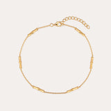The Bamboo Chain Anklet in Gold features delicate cylindrical bar accents, crafted with 18k gold plating and an adjustable clasp with extension chain for the perfect fit.
