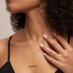 A woman in a black spaghetti strap top showcases the Bamboo Chain Y-Bar Lariat Necklace in Gold and a gold ring. Her manicured hand rests on her chest, drawing attention to her elegant jewelry and neckline.