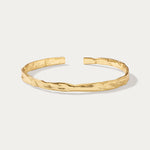 The Elodie Textured Torque Bangle in Gold is a sleek, open bracelet with a polished finish and lava-inspired texture, shown on a plain white background.