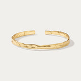 The Elodie Textured Torque Bangle in Gold is a sleek, open bracelet with a polished finish and lava-inspired texture, shown on a plain white background.