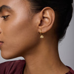 A woman with smooth skin and dark hair pulled back wears the Defender Evil Eye Hoops in Gold. She is dressed in a maroon top and shown in profile against a neutral background.