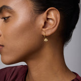 A woman with smooth skin and dark hair pulled back wears the Defender Evil Eye Hoops in Gold. She is dressed in a maroon top and shown in profile against a neutral background.