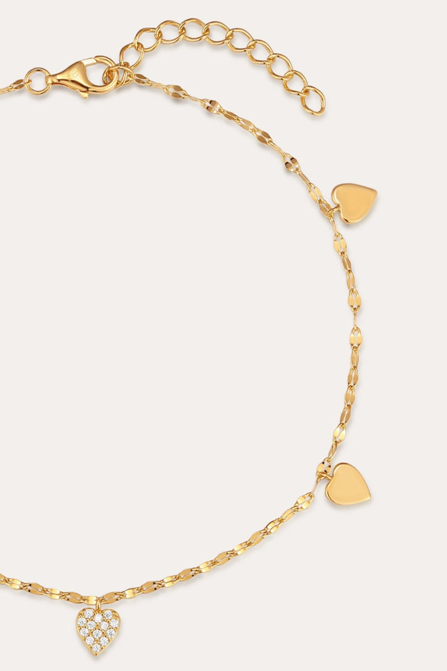 The Louise Gold Heart Anklet features four small gold hearts and a central heart with clear stones on a delicate gold chain. With an adjustable clasp, it can also be worn as a bracelet. Displayed on a plain light background.
