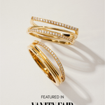 The Noor Pavé Triple Band Ring in Gold features overlapping bands and sparkling white gemstones, with one elegant pavé band. Shown on a light surface with shadows. Text below reads Featured in Vanity Fair.