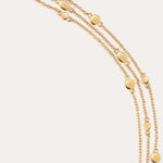 The Simone Triple Chain Layered Bracelet in Gold features three delicate 18k gold plated chains with small gold discs, secured by a toggle and lobster clasp, elegantly displayed on a plain light background.