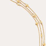 The Simone Triple Chain Layered Bracelet in Gold features three delicate 18k gold plated chains with small gold discs, secured by a toggle and lobster clasp, elegantly displayed on a plain light background.