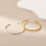 Two bangle bracelets, one with a silver finish and the other with a gold finish, displayed against a neutral background.