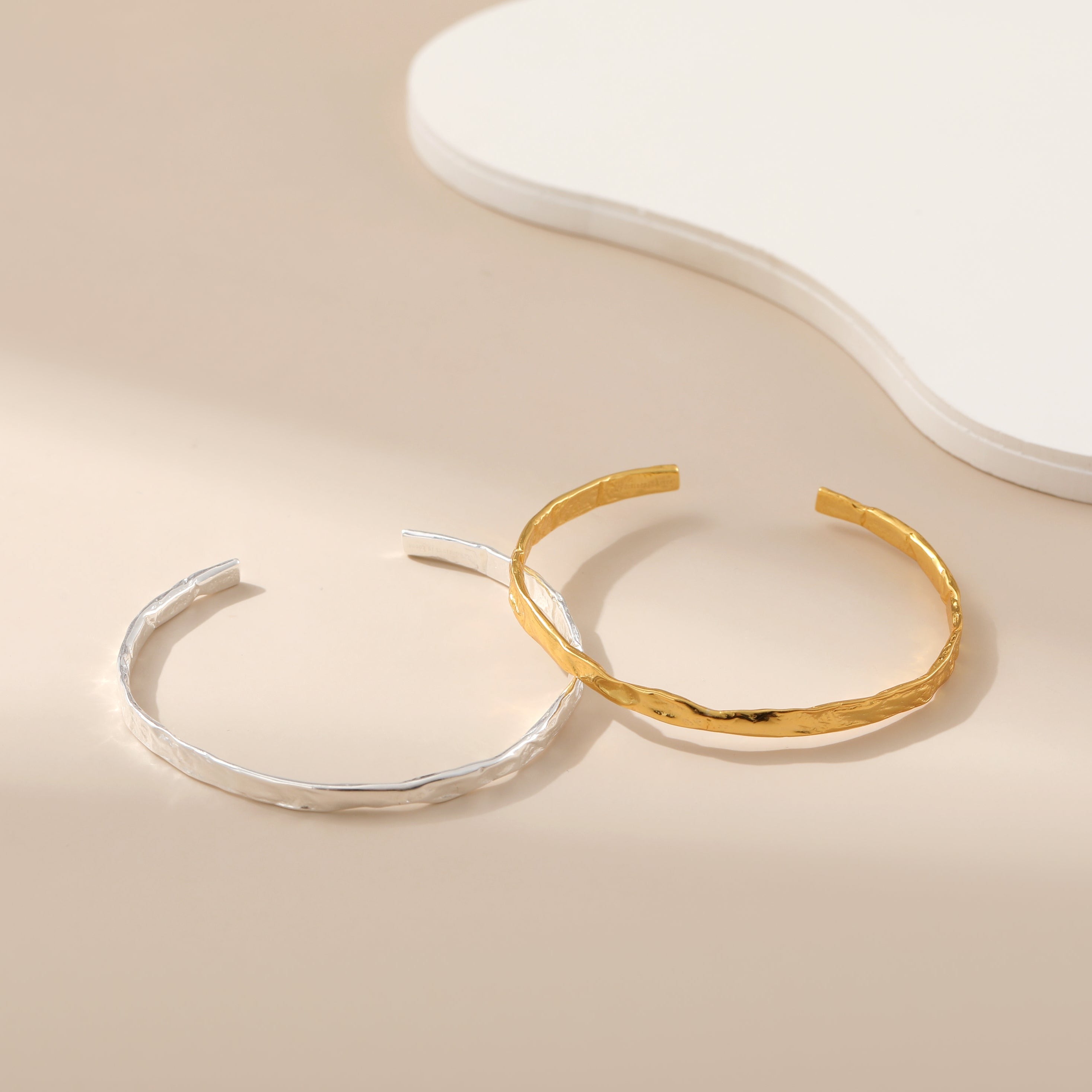 Two bangle bracelets, one with a silver finish and the other with a gold finish, displayed against a neutral background.