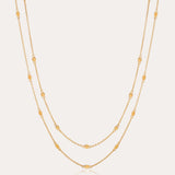 The Simona Double Chain Stacking Necklace in Gold features two delicate chains with evenly spaced oval and round bead accents, making it a minimalist piece thats perfect for layering or wearing solo against a light background.
