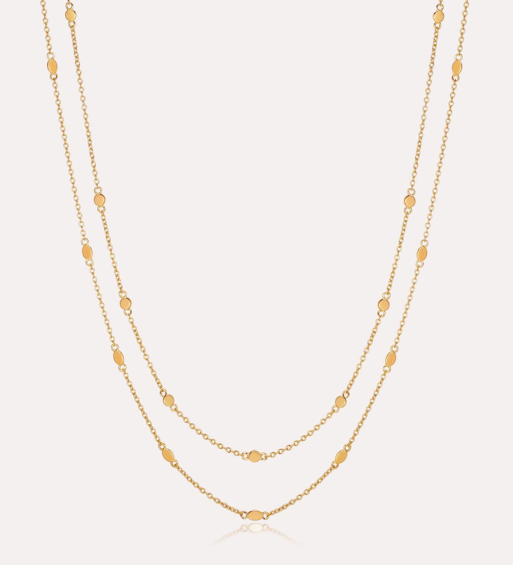 The Simona Double Chain Stacking Necklace in Gold features two delicate chains with evenly spaced oval and round bead accents, making it a minimalist piece thats perfect for layering or wearing solo against a light background.