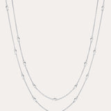 The Simona Double Chain Stacking Necklace in Silver features two delicate layers with small, evenly spaced beads along each chain, shown against a light background.