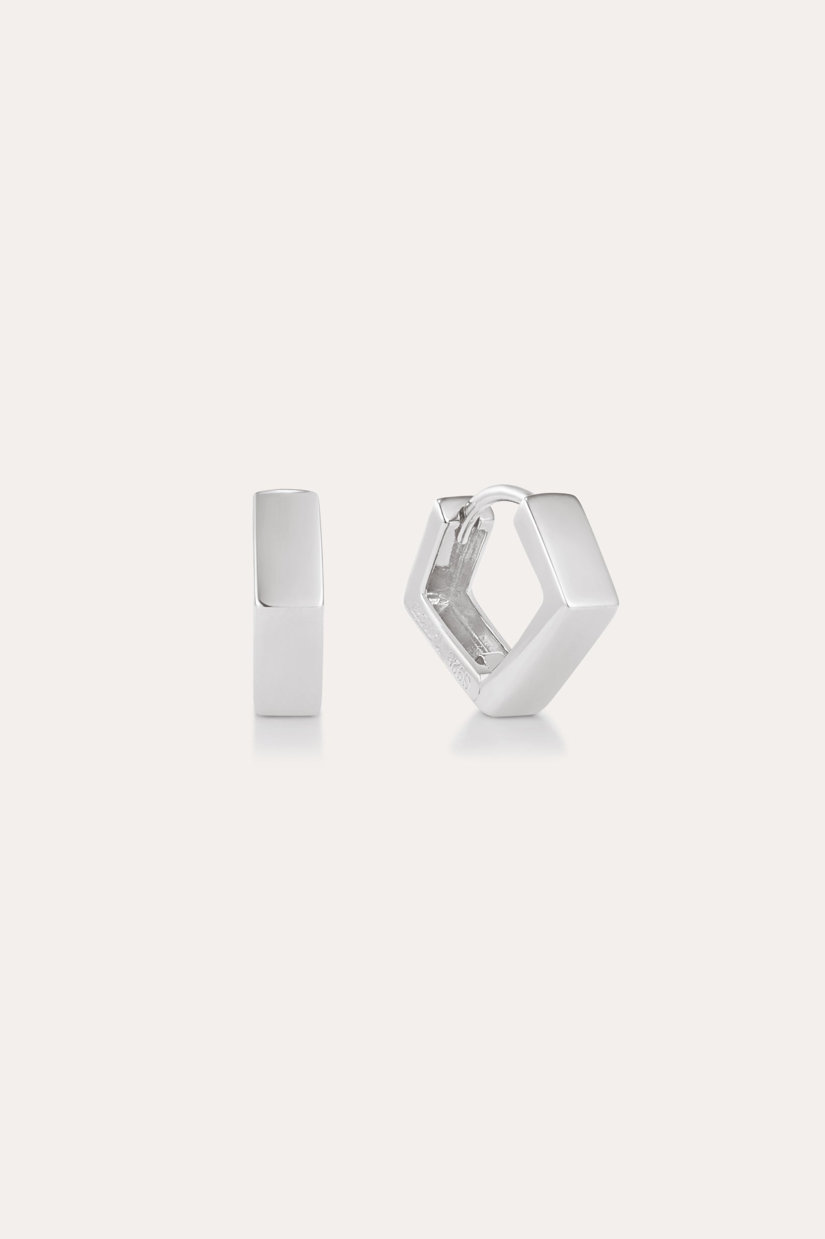 The Judith Hexagon Angular Huggies in Silver, featuring a chunky geometric design, are shown on a plain light background—one upright and one open to reveal the clasp. Perfect for stacking earring looks.