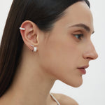 A woman with straight dark hair, in a white thin-strap top, is shown in profile wearing sterling silver ear cuffs and Juni Pavé Chunky Hoop Earrings in Silver on her left ear, against a plain white background.