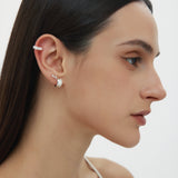 A woman with straight dark hair, in a white thin-strap top, is shown in profile wearing sterling silver ear cuffs and Juni Pavé Chunky Hoop Earrings in Silver on her left ear, against a plain white background.