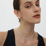 A woman with slicked-back brown hair wears a sleeveless black top and Juno Ridged Chunky Hoops in Silver, looking confidently at the camera against a plain white background.