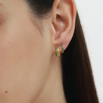 Close-up of a womans ear with two gold hoops—one plain, one Kiki Crystal Huggie Earring in Gold/Green. She has straight, dark hair and smooth skin, set against a light background.