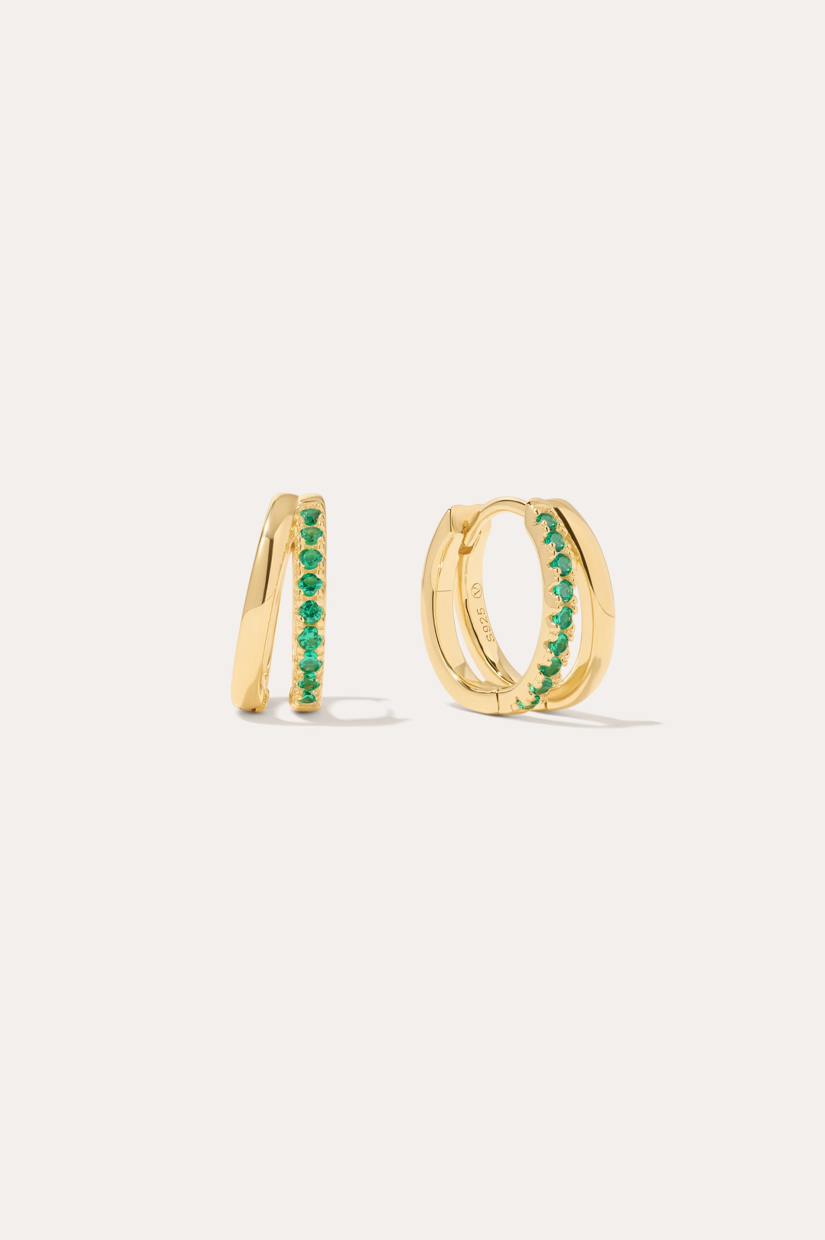 The Kira Crystal Double Hoop Huggies in Gold/Green are small earrings featuring a row of shimmering gemstones on the front, displayed against a plain light background.