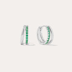 The Kira Crystal Double Hoop Huggies in Sterling Silver/Green feature a row of green gemstones along the front and are displayed against a plain white background.