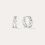 The Kira Crystal Double Hoop Huggies in Sterling Silver are shown, each featuring a row of sparkling round crystals along the front edge. The background is plain and light-colored.