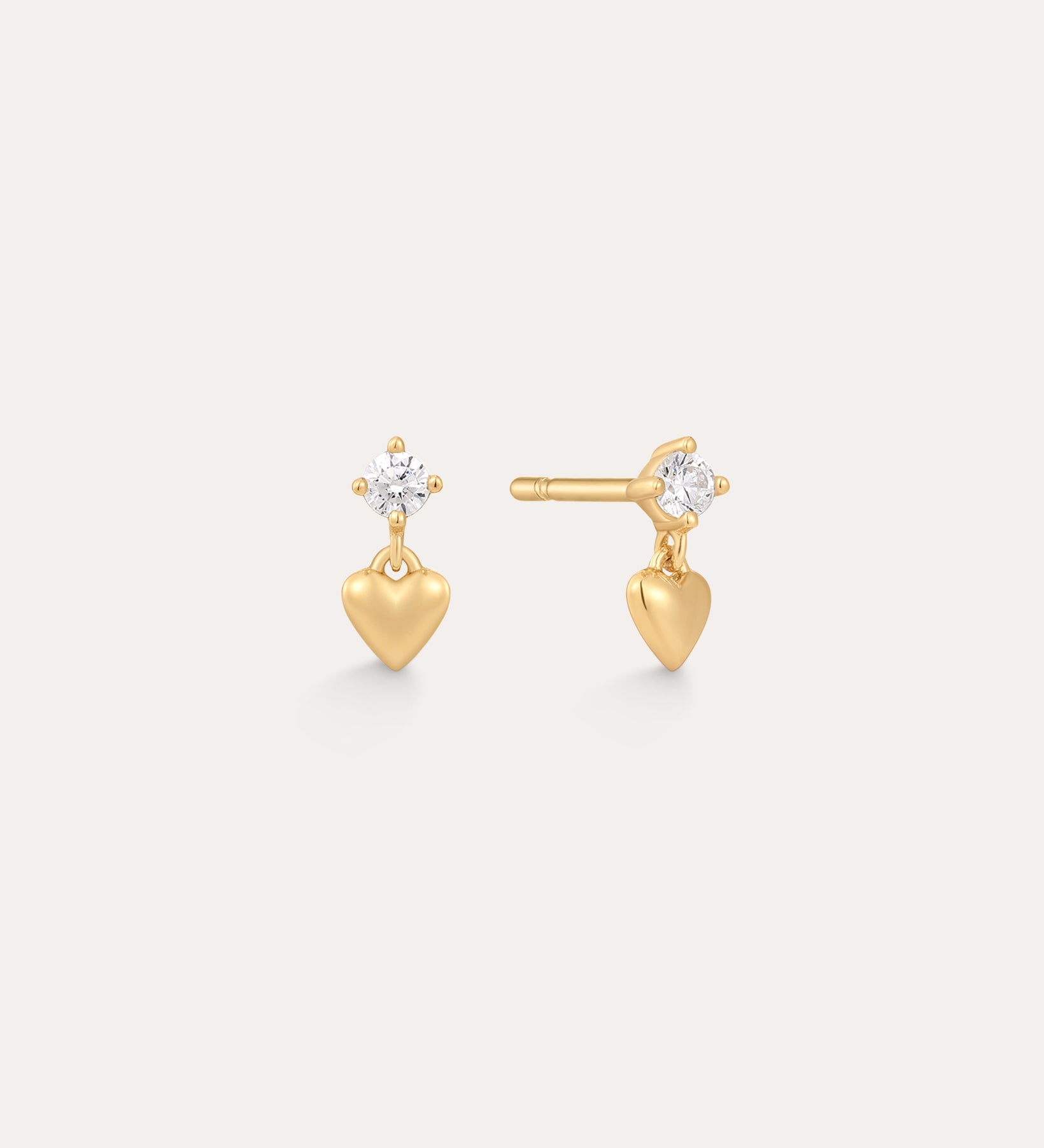 The Lilian Crystal Heart Studs Earrings in Gold feature a small gold heart charm dangling below a sparkling round crystal, displayed on a plain light background.