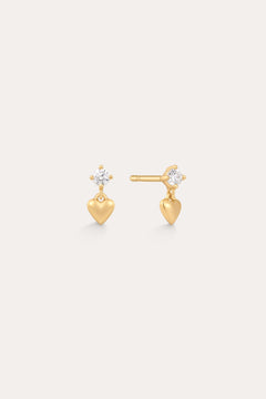 The Lilian Crystal Heart Studs Earrings in Gold feature a small gold heart charm dangling below a sparkling round crystal, displayed on a plain light background.