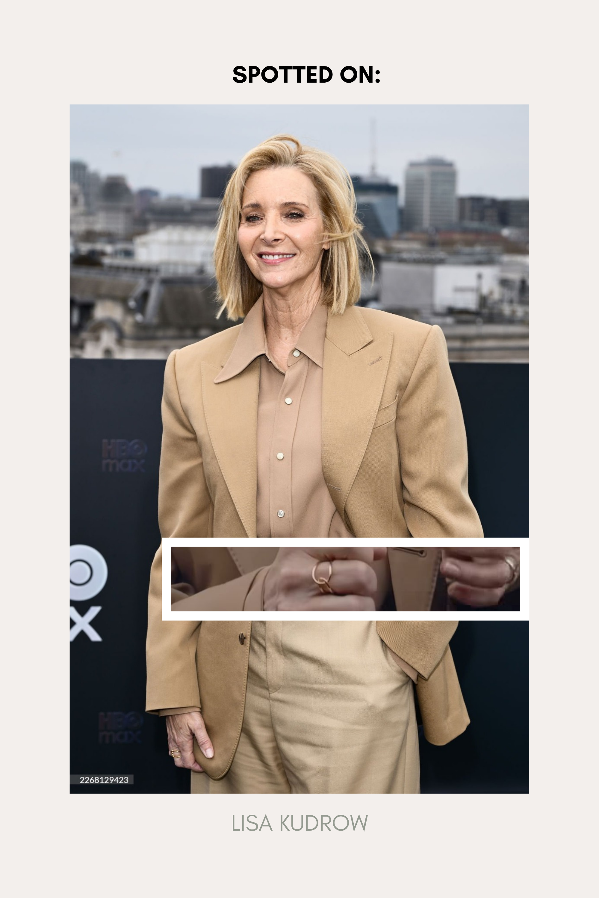 A woman with short blonde hair smiles outdoors in a city, wearing a beige blazer over a matching blouse and the Ayla Link Ring in Gold. Text above reads SPOTTED ON: and below, LISA KUDROW.