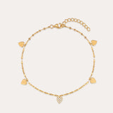 The Louise Gold Heart Anklet features a delicate gold chain with small heart charms, including a central charm adorned with clear stones. It has an adjustable chain and lobster clasp closure.