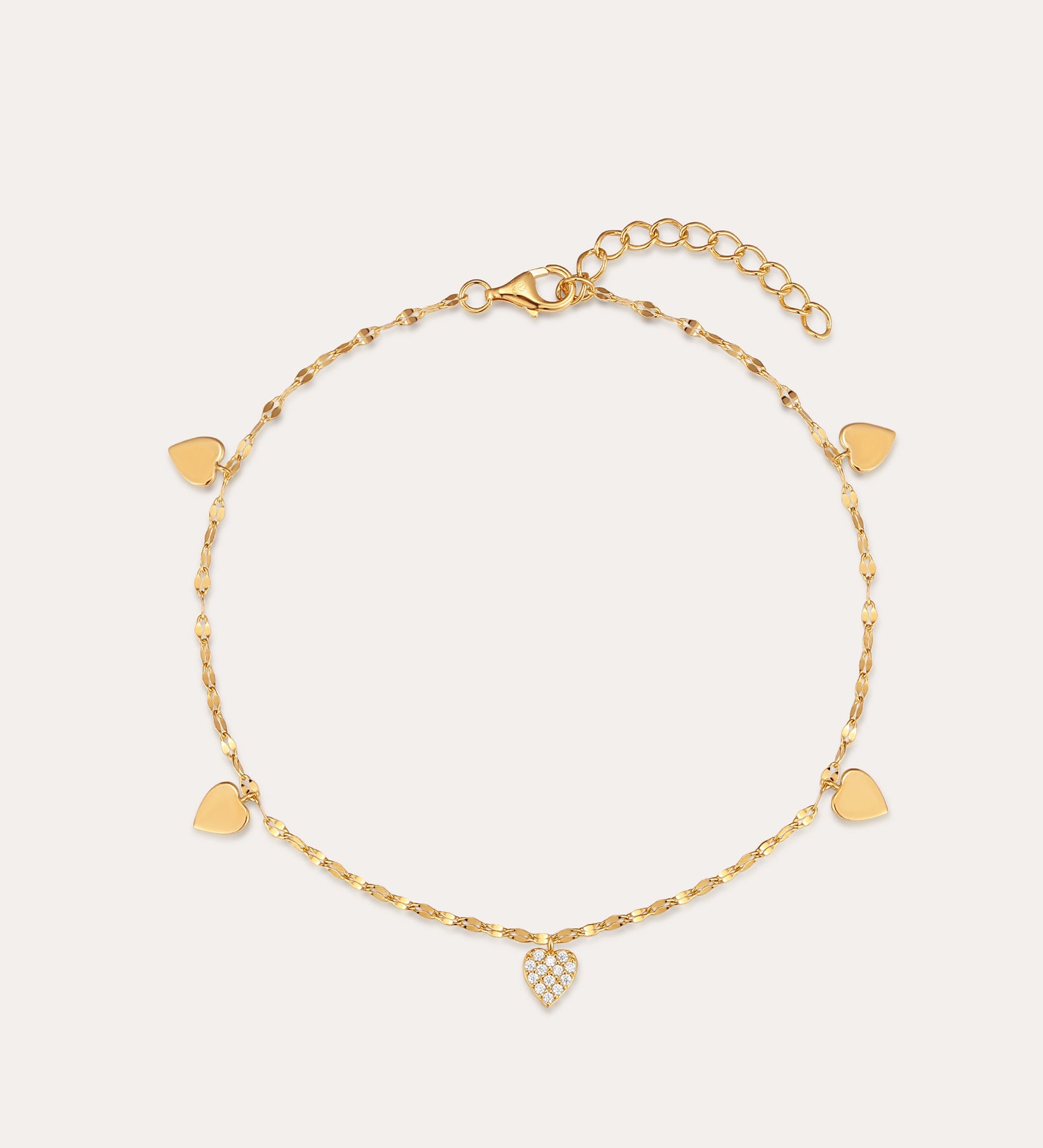 The Louise Gold Heart Anklet features a delicate gold chain with small heart charms, including a central charm adorned with clear stones. It has an adjustable chain and lobster clasp closure.