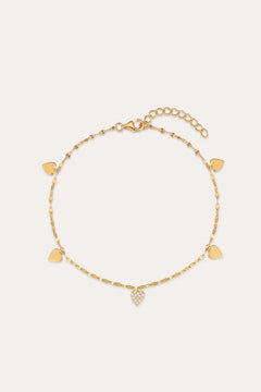 The Louise Gold Heart Anklet features a delicate gold chain with small heart charms, including a central charm adorned with clear stones. It has an adjustable chain and lobster clasp closure.